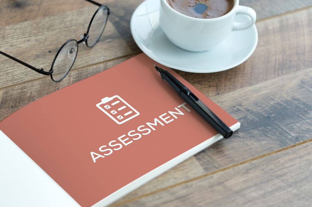 Desk with coffee, glasses a pen and an assessment book