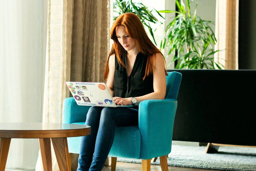 Woman sat in a communal space working with a laptop on her lap