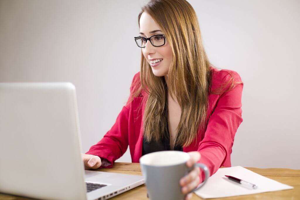 Woman in red jacket with a cup of tea working on laptop