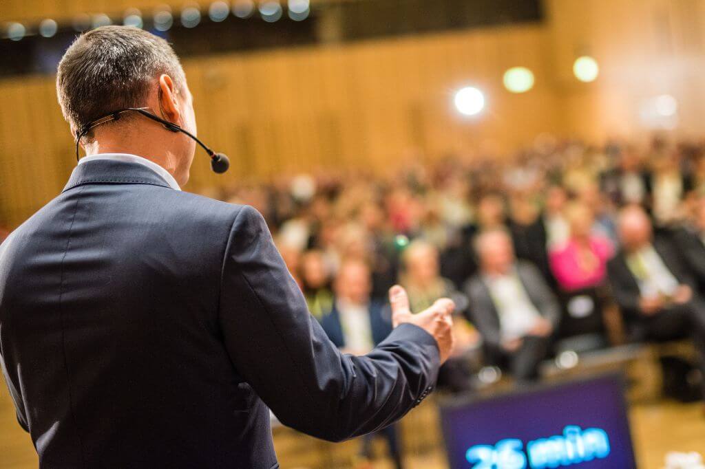 Man from behind speaking at a conference full of people