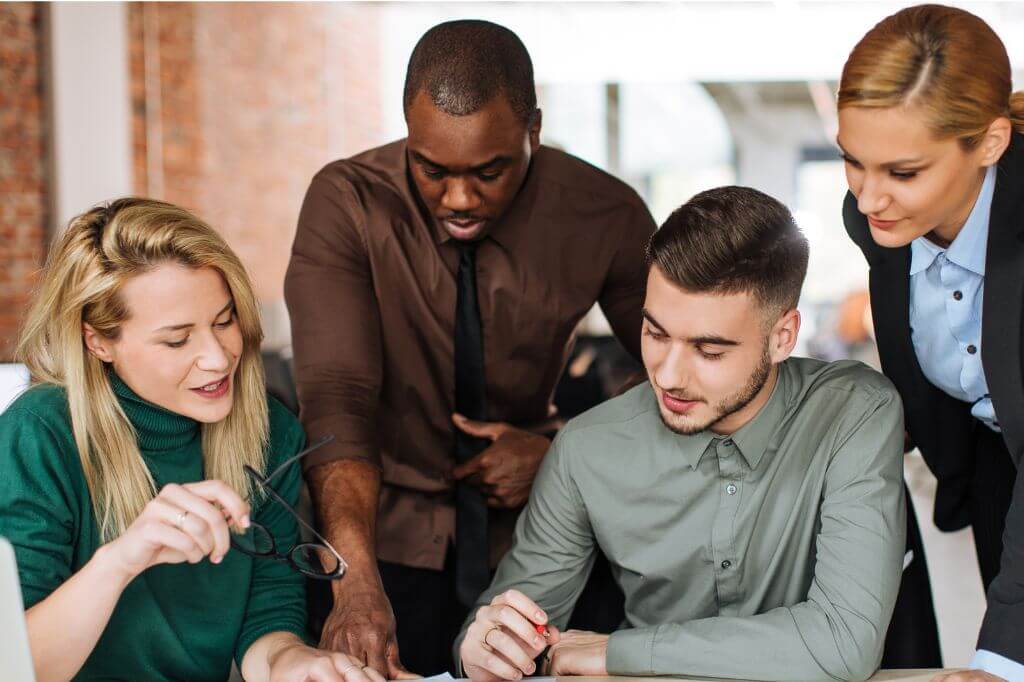 Two men and two women in an office huddled over some paperwork discussing