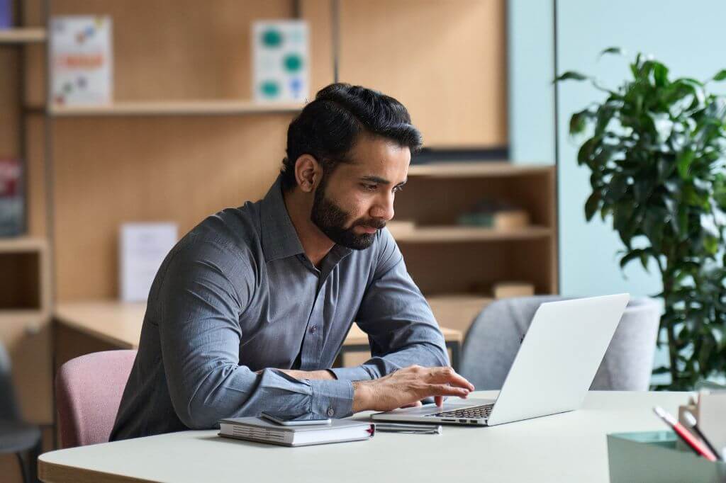 Man in office, deep in thought working on laptop